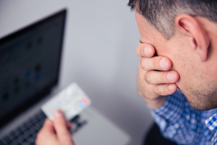 Upset man holding credit card with laptop on background-1